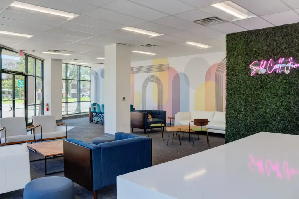 Community Corner lounge with colorful geometric wall art and a neon sign on a greenery wall