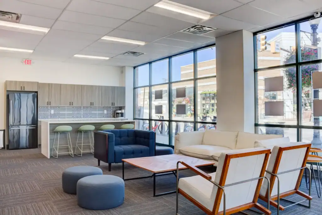 Lounge with sofas, chairs, coffee table, and a kitchenette with bar stools and a large window view