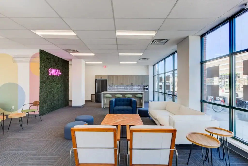 Lounge area with sofas, chairs, tables, a green wall, neon sign, and large windows