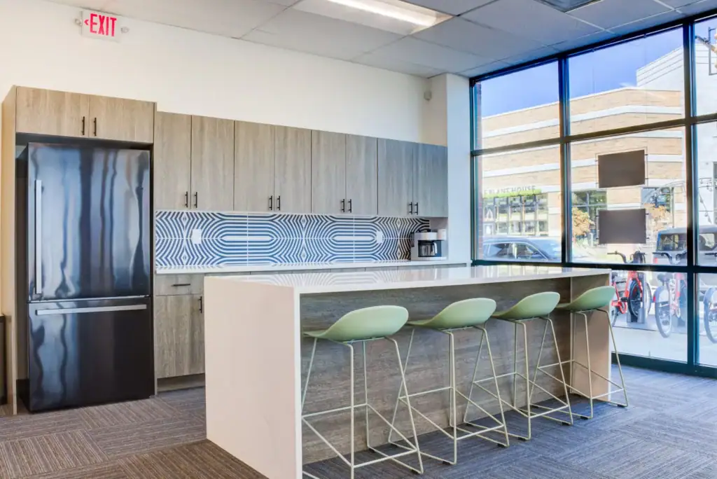 Kitchen with wooden cabinets, black refrigerator, geometric backsplash, white countertop island, and green bar stools