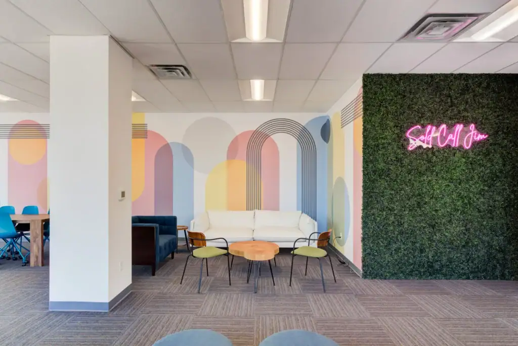 Lounge with colorful geometric wall art, white sofa, chairs, and a neon sign on a green wall
