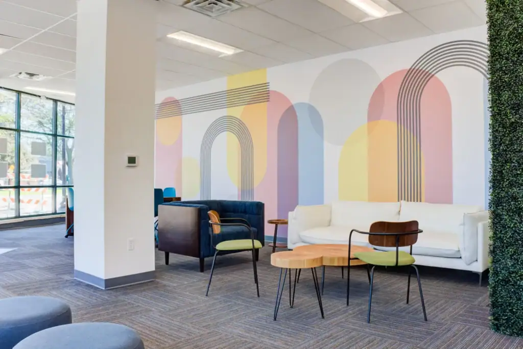 Lounge area with colorful wall art, white couch, chairs, wooden tables, and a green plant wall